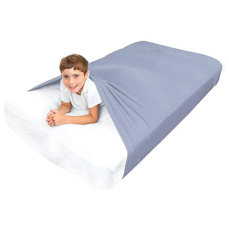 Child smiling under gray sensory compression sheet on white mattress